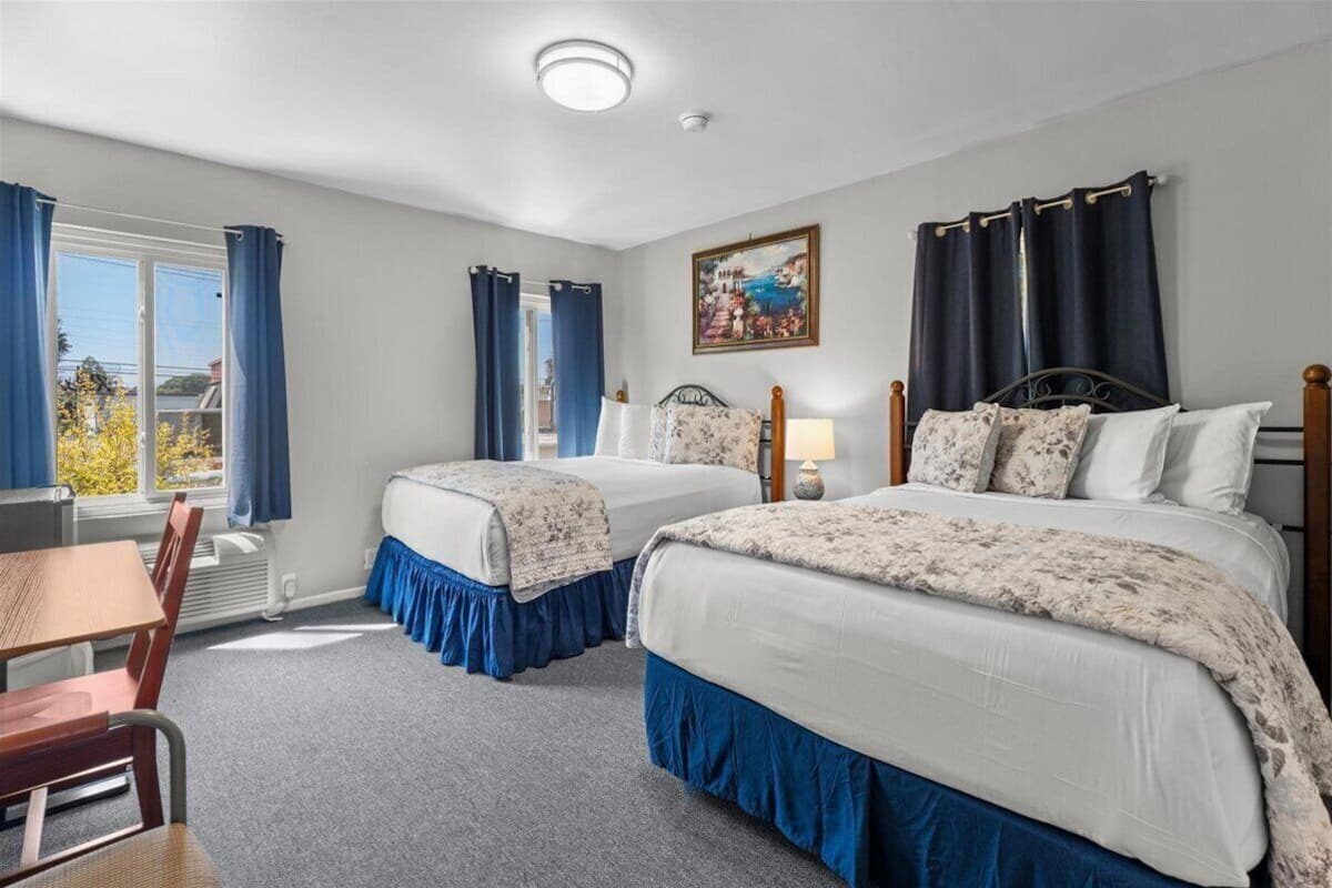 Habitación de hotel con dos camas, una mesa de comedor y una ventana con cortinas.