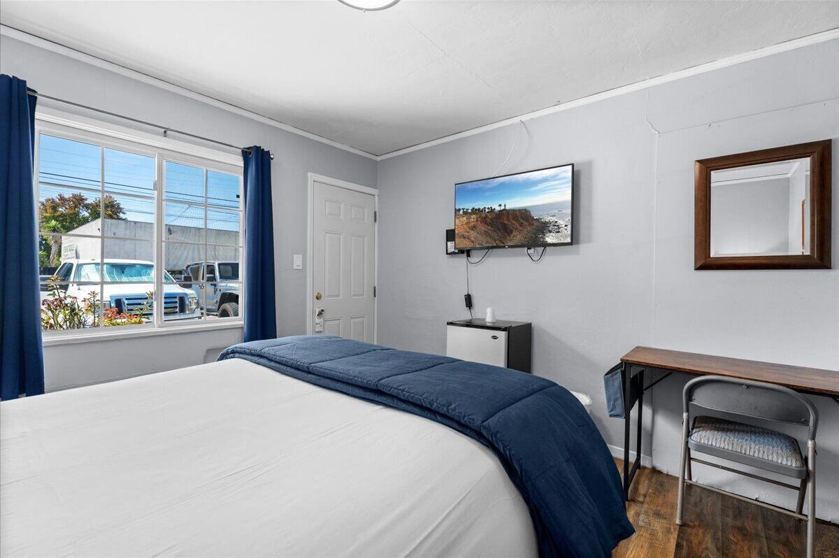 Un dormitorio con cama, escritorio, silla, televisor y ventana con cortinas.