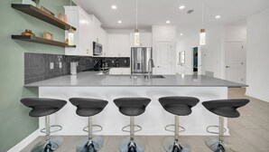 A modern kitchen with a central island, bar stools, and built-in appliances. - EV_9282 - 7 Bed 5 Bath Villa with Screened Private Pool, Spillover Spa, Kids Bed (Davenport)