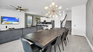 A modern kitchen with a central island, a dining area with a long table, and a living room with a large sofa and a TV. - EV_9282 - 7 Bed 5 Bath Villa with Screened Private Pool, Spillover Spa, Kids Bed (Davenport)