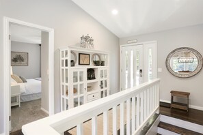 Una escalera con barandilla blanca conduce a un dormitorio con una cama y un armario blanco con adornos.