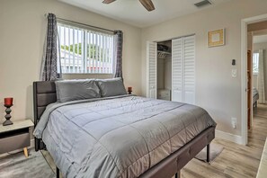 Een slaapkamer met een bed, nachtkastje, raam met gordijnen, kast en deur naar een andere kamer.