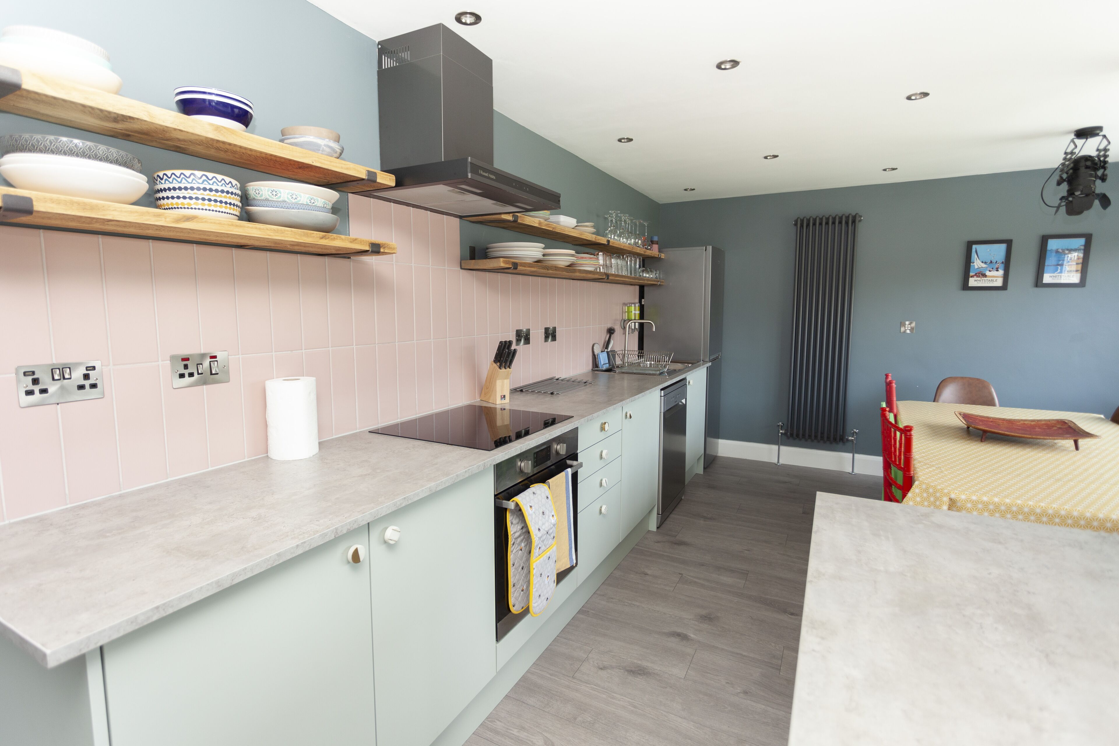 A modern kitchen with light-colored cabinets, wooden shelves, and a built-in oven.