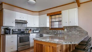 Cozinha com armários brancos, bancada de granito, eletrodomésticos de aço inoxidável e ilha de madeira com banquetas.