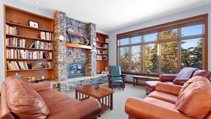 A living room with leather sofas, a stone fireplace, bookshelves, and large windows with a view of trees. - Missoula Family Retreat (Missoula)