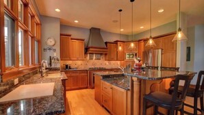 A spacious kitchen with granite countertops, wooden cabinets, and a central island with bar stools. - Missoula Family Retreat (Missoula)