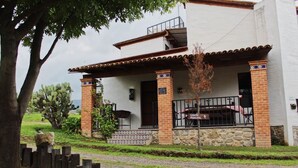 Um edifício de dois andares com varanda coberta, alicerce de pedra e uma placa indicando ser o edifício principal.