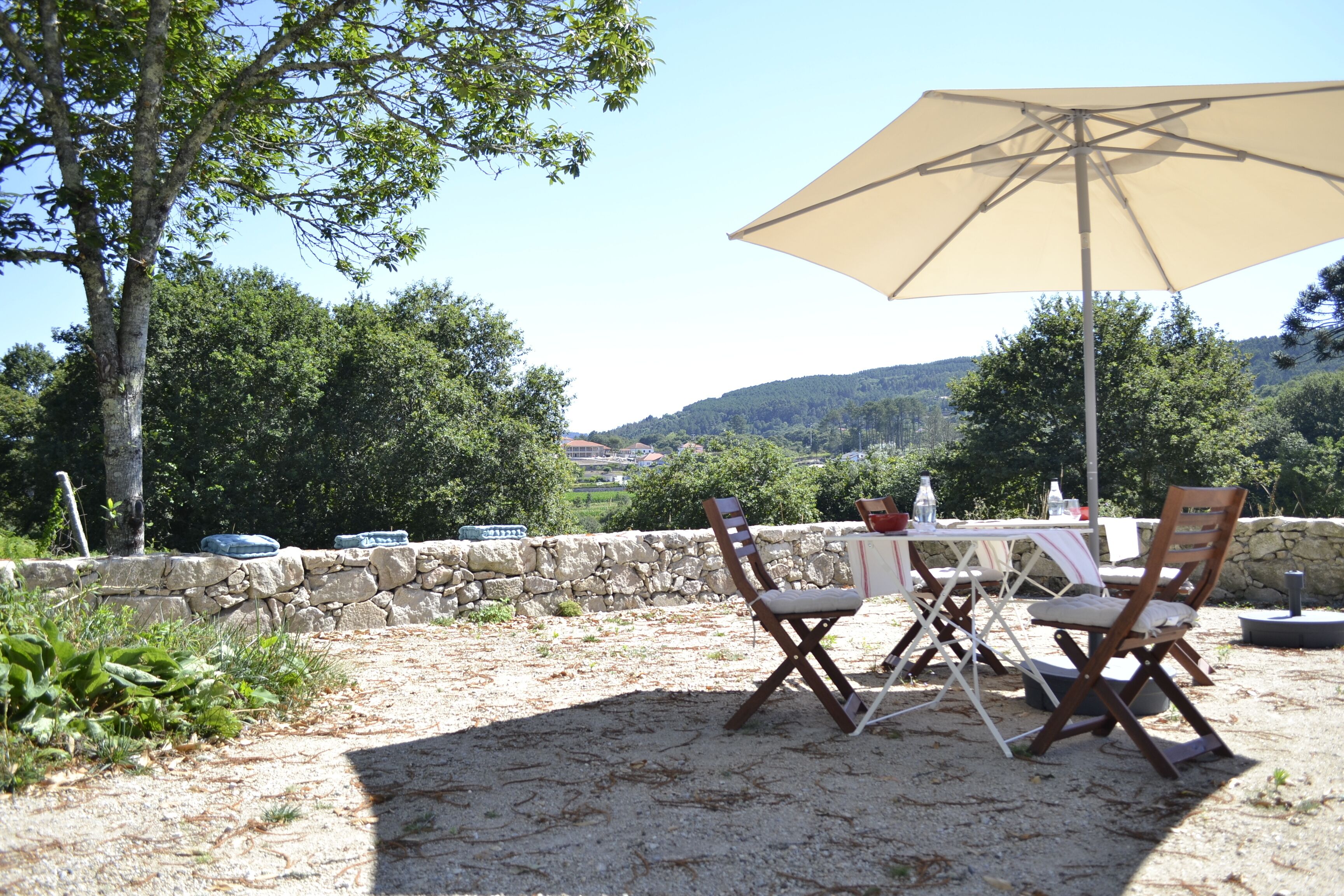 Un patio al aire libre con una mesa, sillas y un gran paraguas, junto a un muro de piedra.