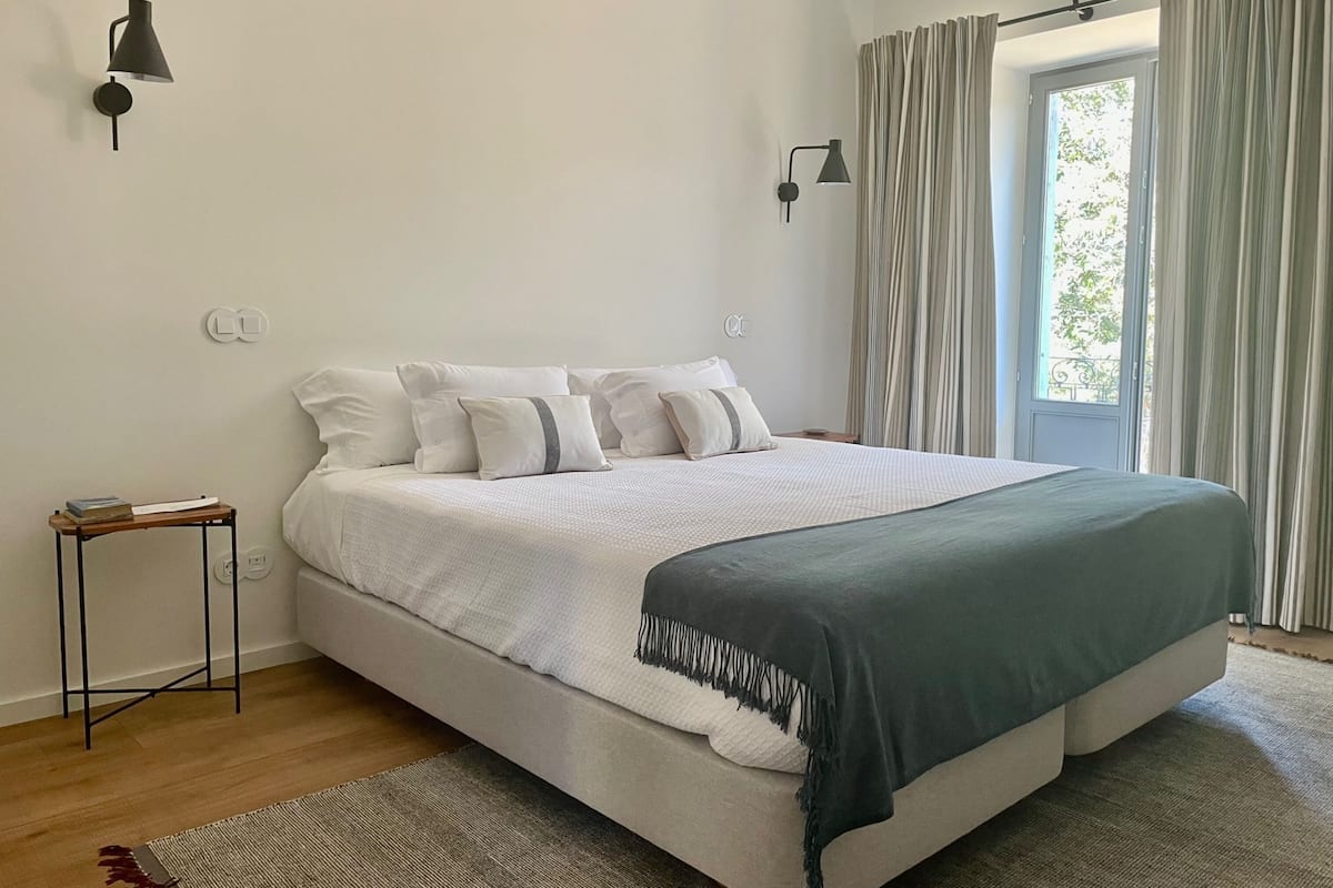 Un dormitorio moderno con una cama grande, una mesita de noche y dos lámparas fijadas a la pared.