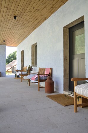 Un espacio al aire libre cubierto con sillas y una mesa de madera, una planta en maceta y una puerta con ventanal.