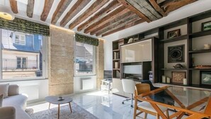 A modern living room with a glass coffee table, a sofa, and a dining table with chairs. There are bookshelves and a TV mounted on the wall. - Parisian Pied-a-terre in the heart of the city - Close to everything (Paris)