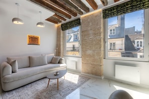 Un salon moderne avec un canapé, une table basse et une vue sur les immeubles à travers de grandes fenêtres.