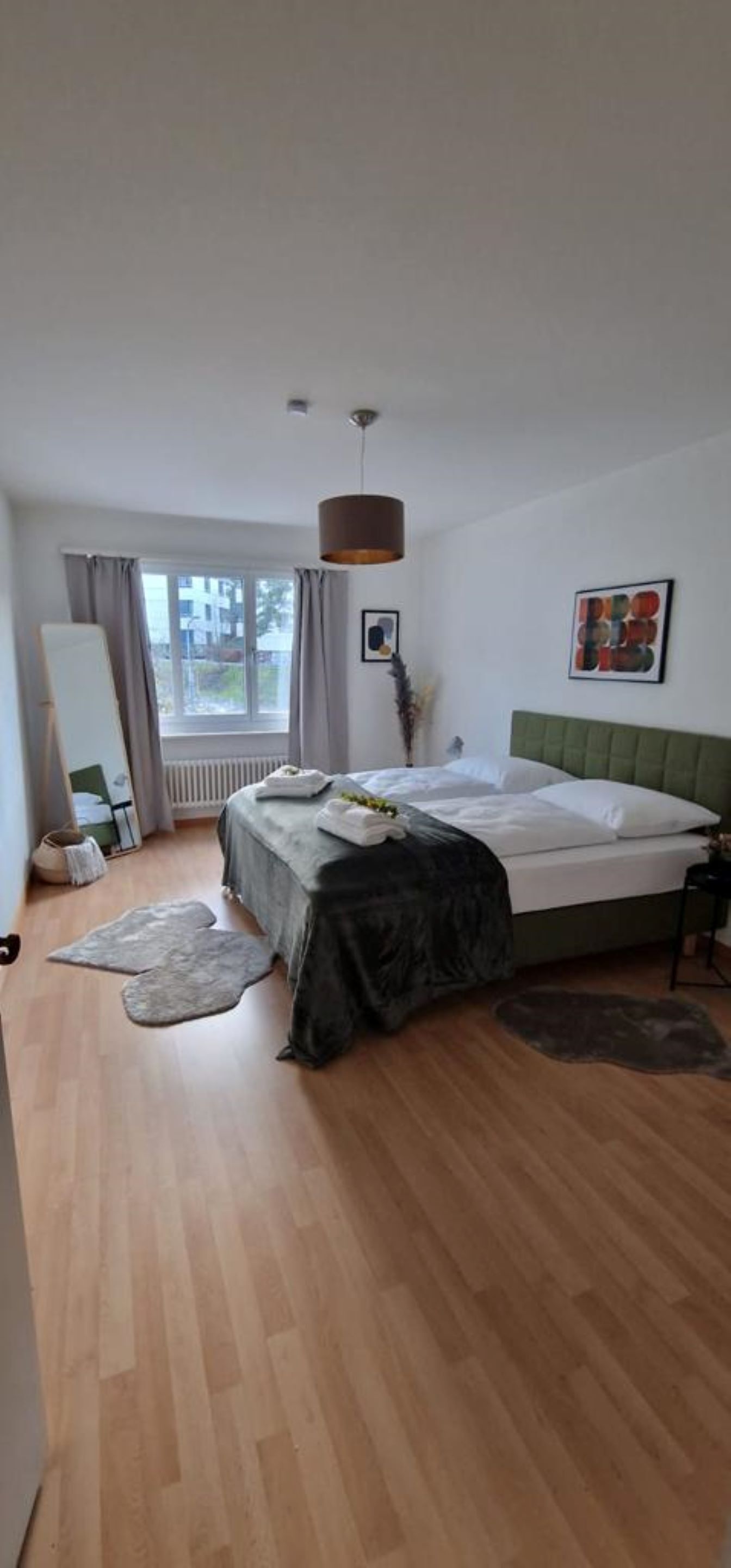 A bedroom with a bed, a hanging light fixture, a window with curtains, and a view of the outside.