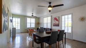 A spacious dining area with a large table and chairs, a ceiling fan, and large windows providing natural light. - El Flamingo Beach Club (Manati)