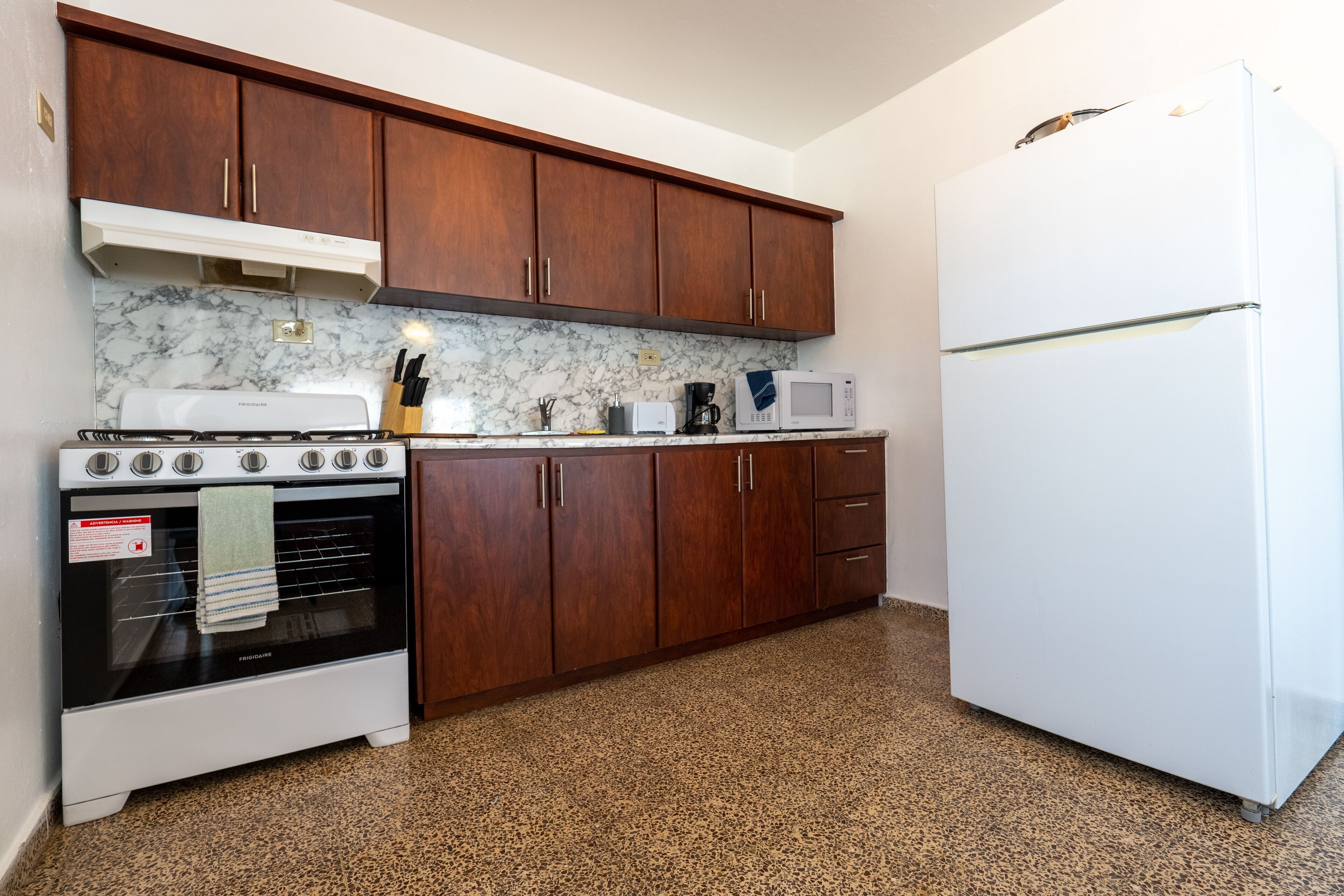 Una cocina con armarios de madera, un refrigerador blanco, una estufa y un microondas.