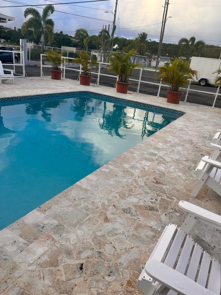A swimming pool with stone tiles and white lounge chairs.