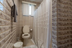 A bathroom with a toilet, a shower curtain, and a small trash bin.