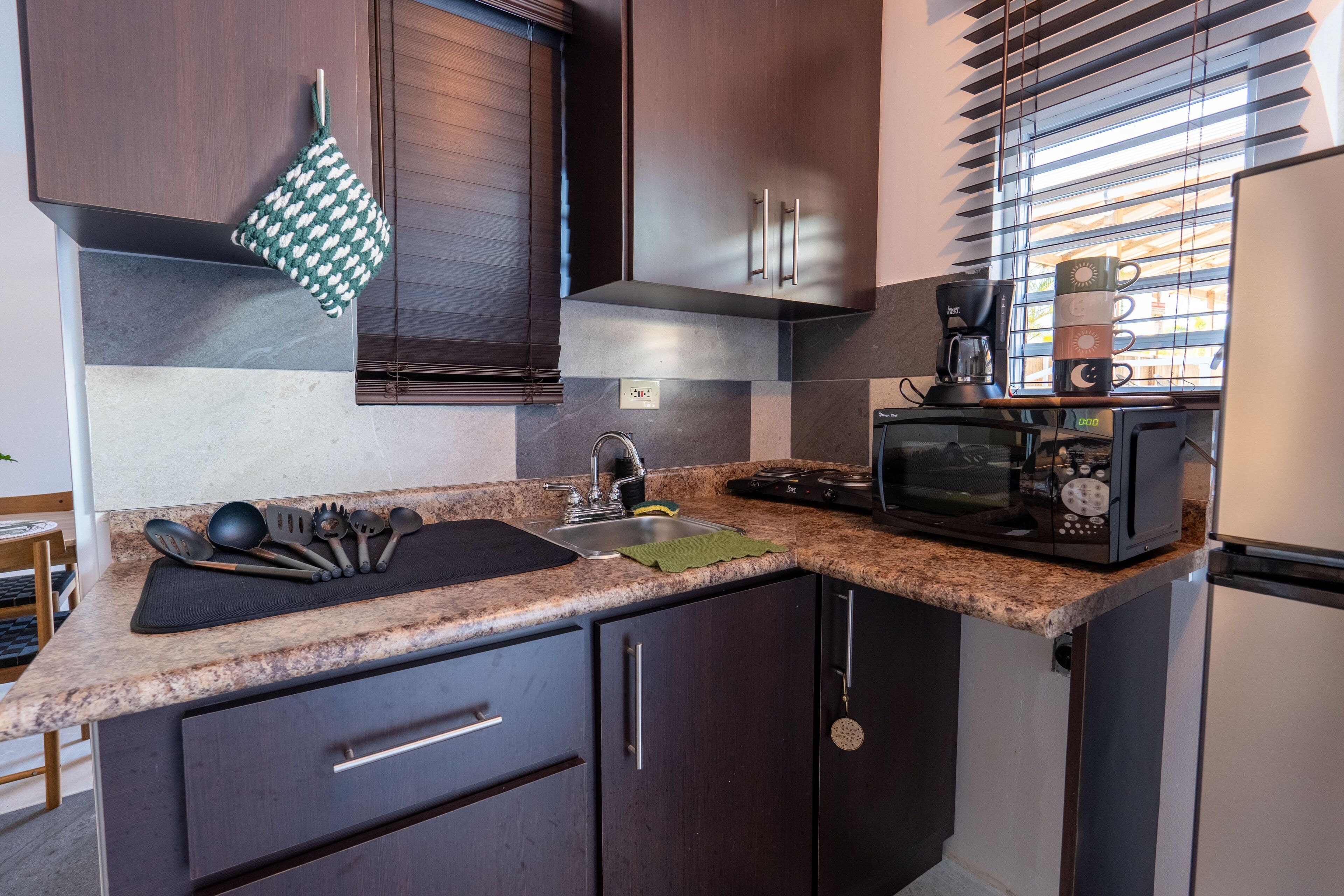 A compact kitchen with dark wood cabinets, a granite countertop, a coffee maker, and a microwave.