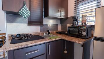 A compact kitchen with dark wood cabinets, a granite countertop, a coffee maker, and a microwave.