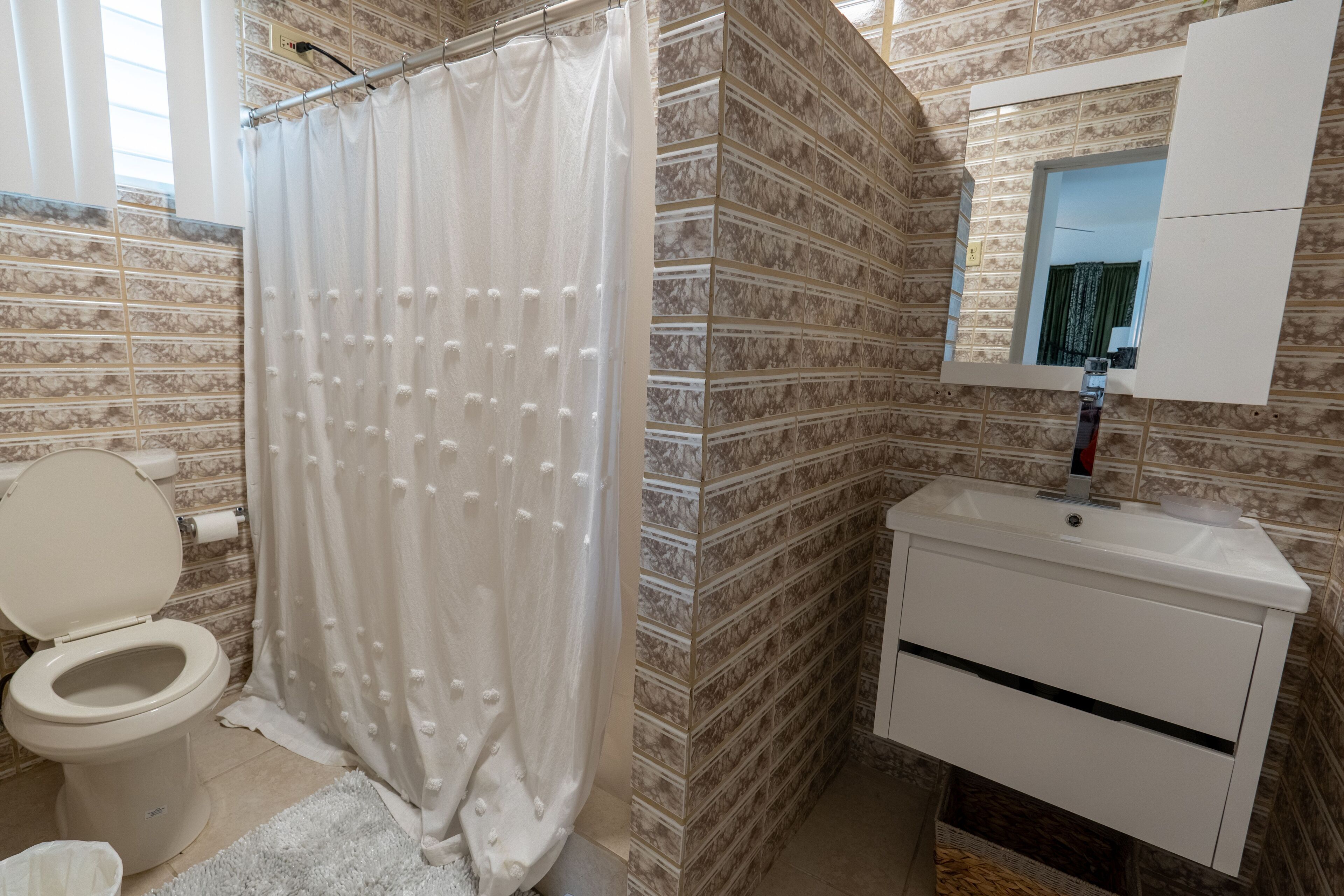 A bathroom with a toilet, shower curtain, sink, and mirror.