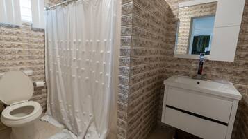 Une salle de bain équipée de toilettes, d’un rideau de douche, d’un lavabo et d’un miroir.