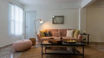 Ett vardagsrum med en soffa, ett soffbord, en golvlampa och ett inramat konstverk på väggen.
