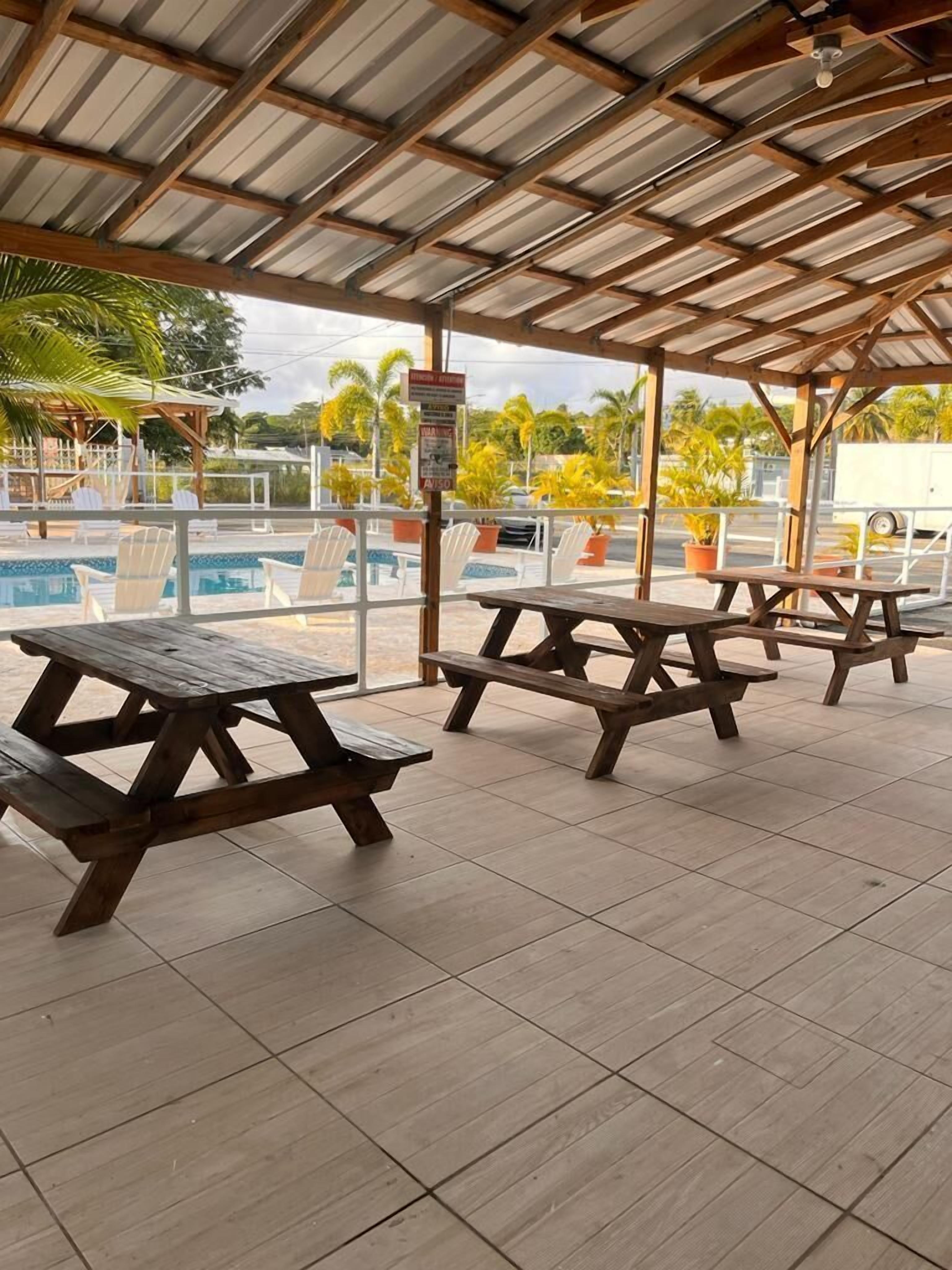 Un espacio al aire libre techado con mesas de picnic y una piscina.