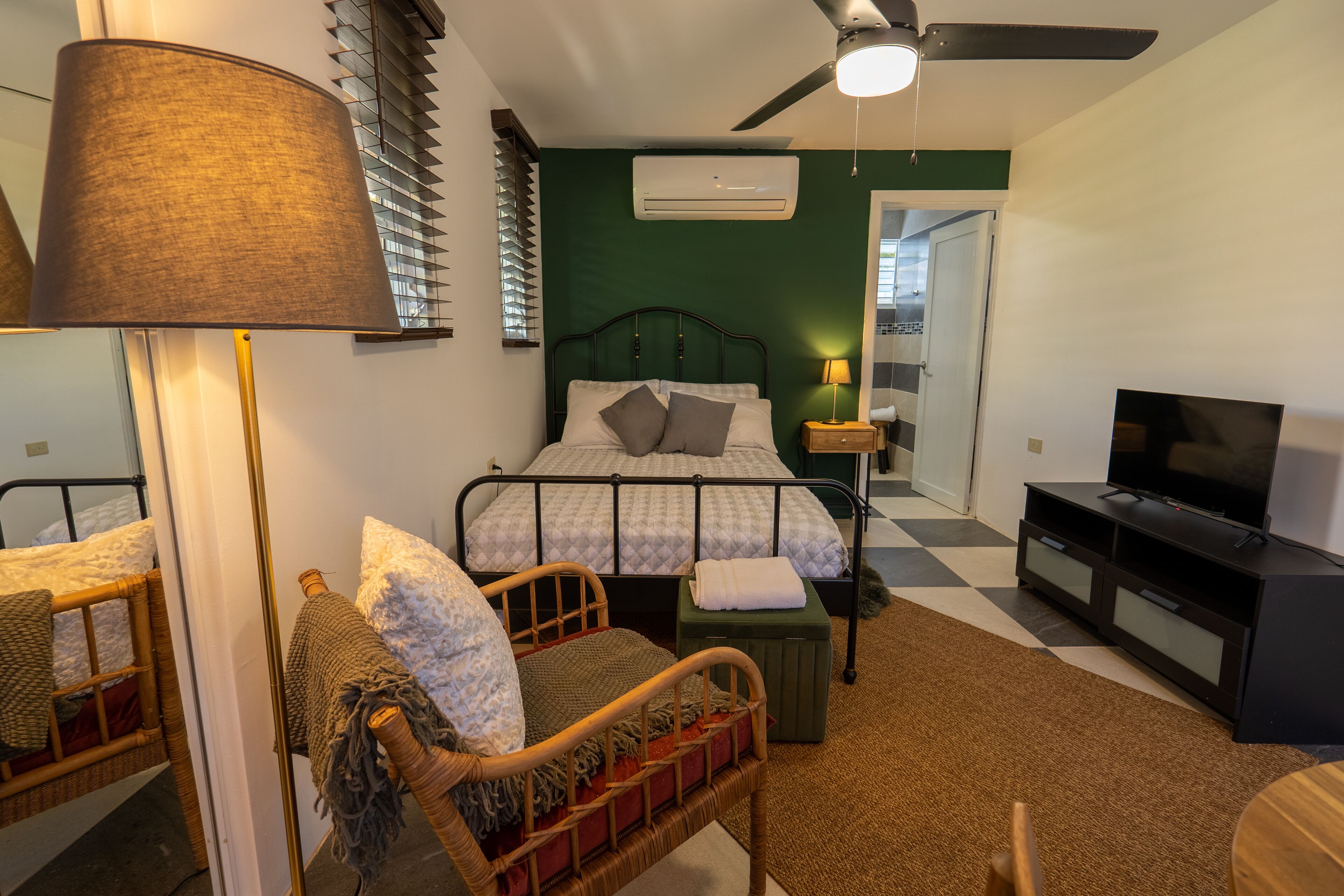 A bedroom with a bed, bedside table, lamp, TV, and a ceiling fan.