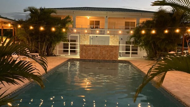 A pool area with a house in the background, surrounded by palm trees and string lights. - El Flamingo Beach Club (Manati)
