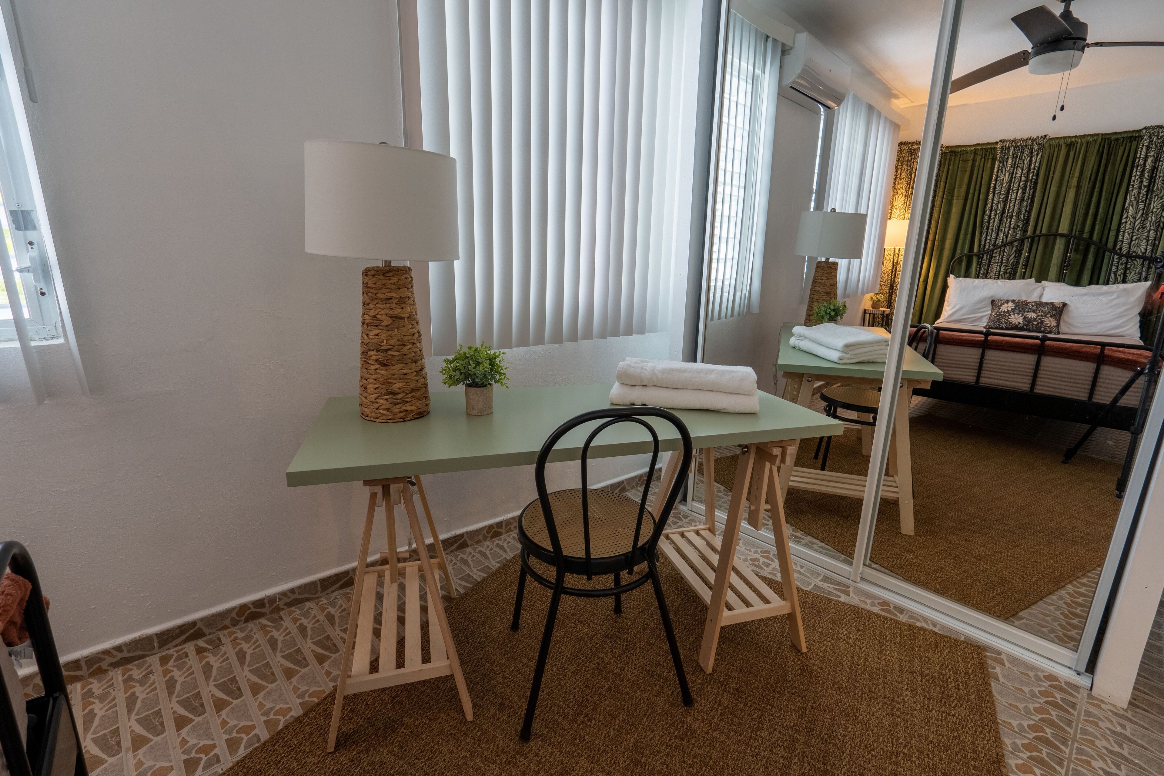 Ein Hotelzimmer mit Bett, Schreibtisch mit Stuhl, Lampe und Fenster mit Jalousien.