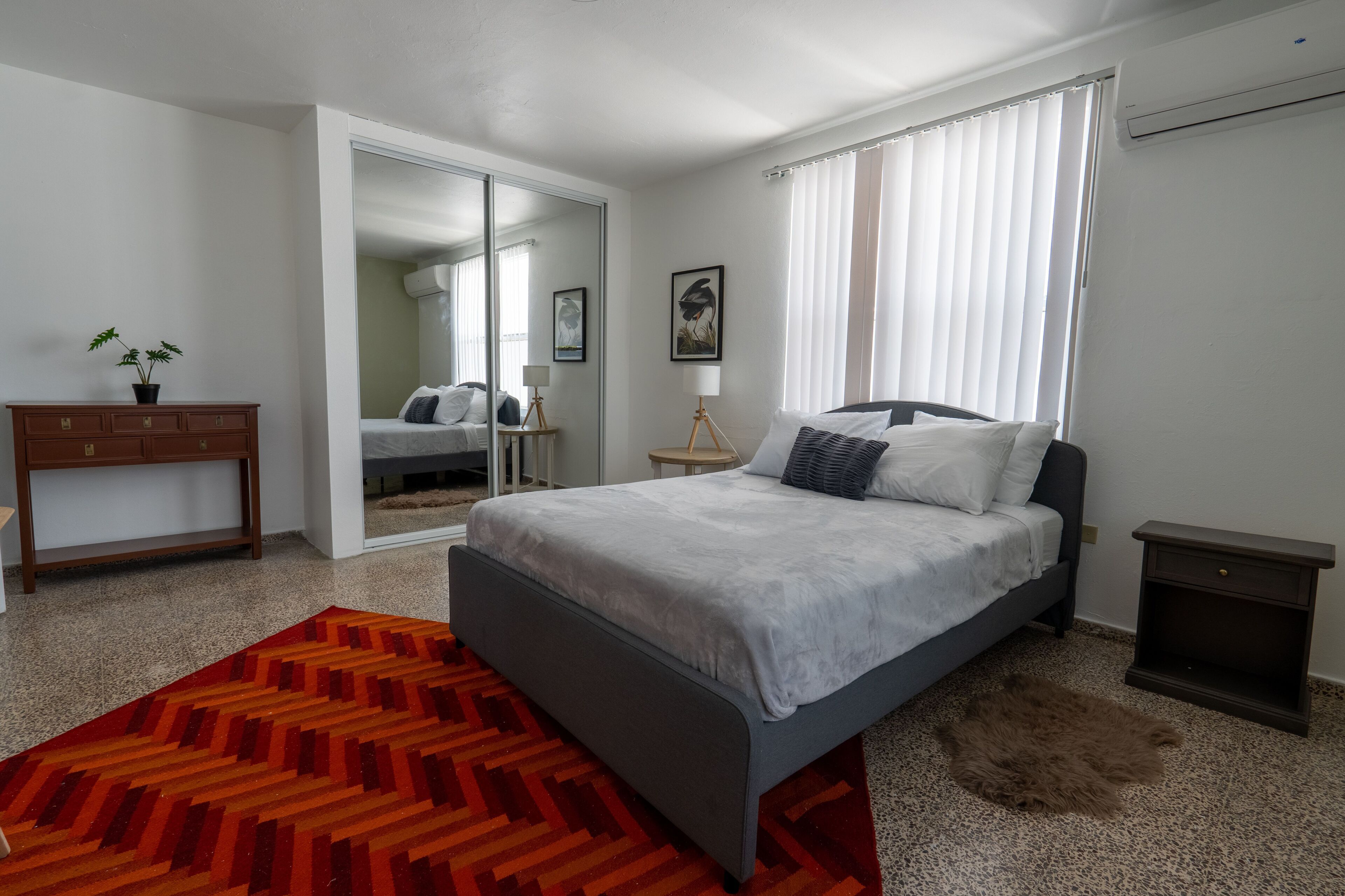 A modern bedroom with a bed, a nightstand, a dresser, and a mirror.