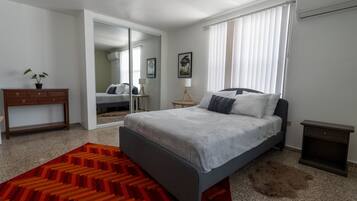 A modern bedroom with a bed, a nightstand, a dresser, and a mirror.