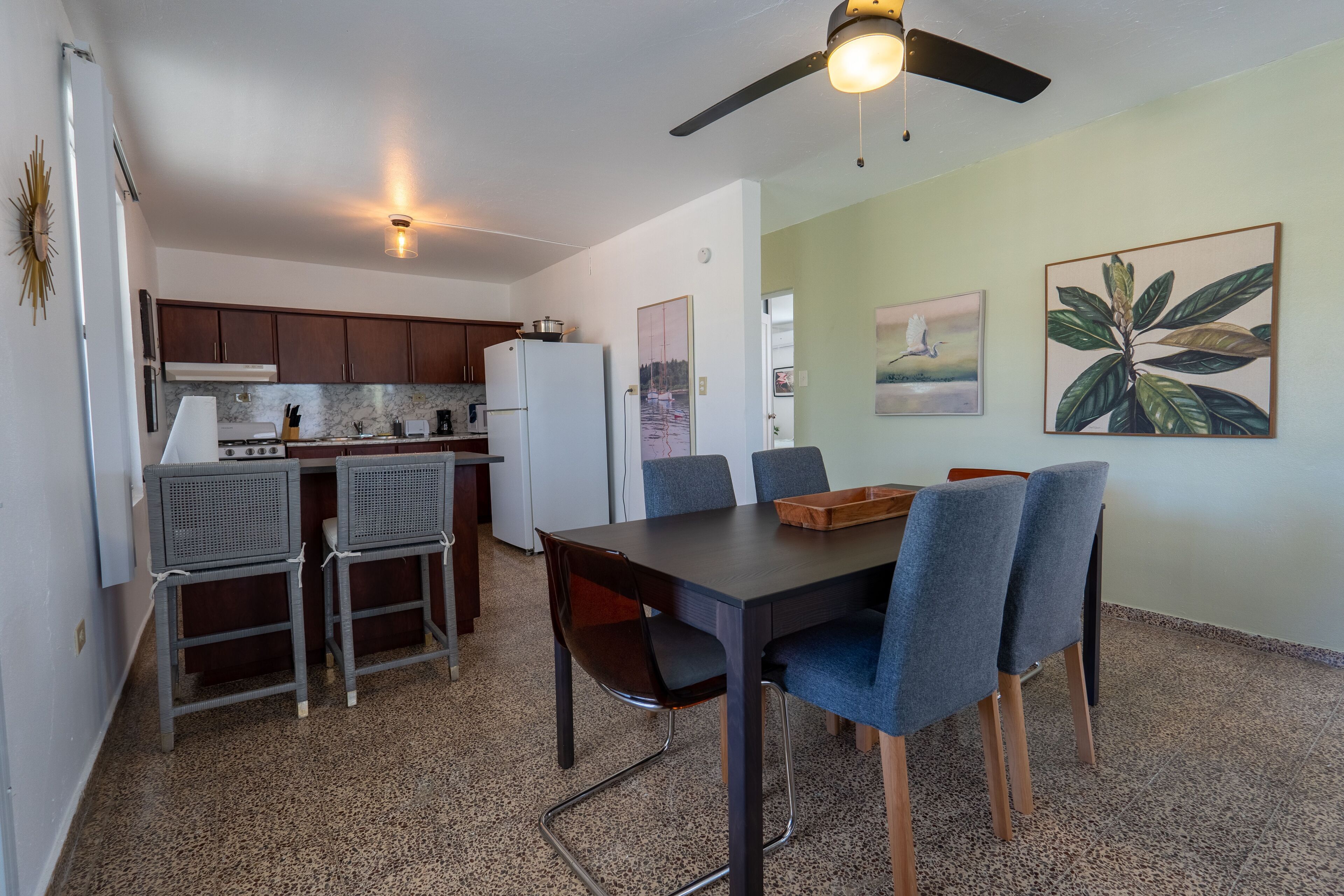A compact kitchen with dark wooden cabinets, a white refrigerator, and a dining area with a table and chairs.