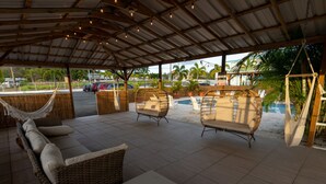 A covered outdoor seating area with wicker furniture, a pool, and a view of the surrounding landscape. - El Flamingo Beach Club (Manati)