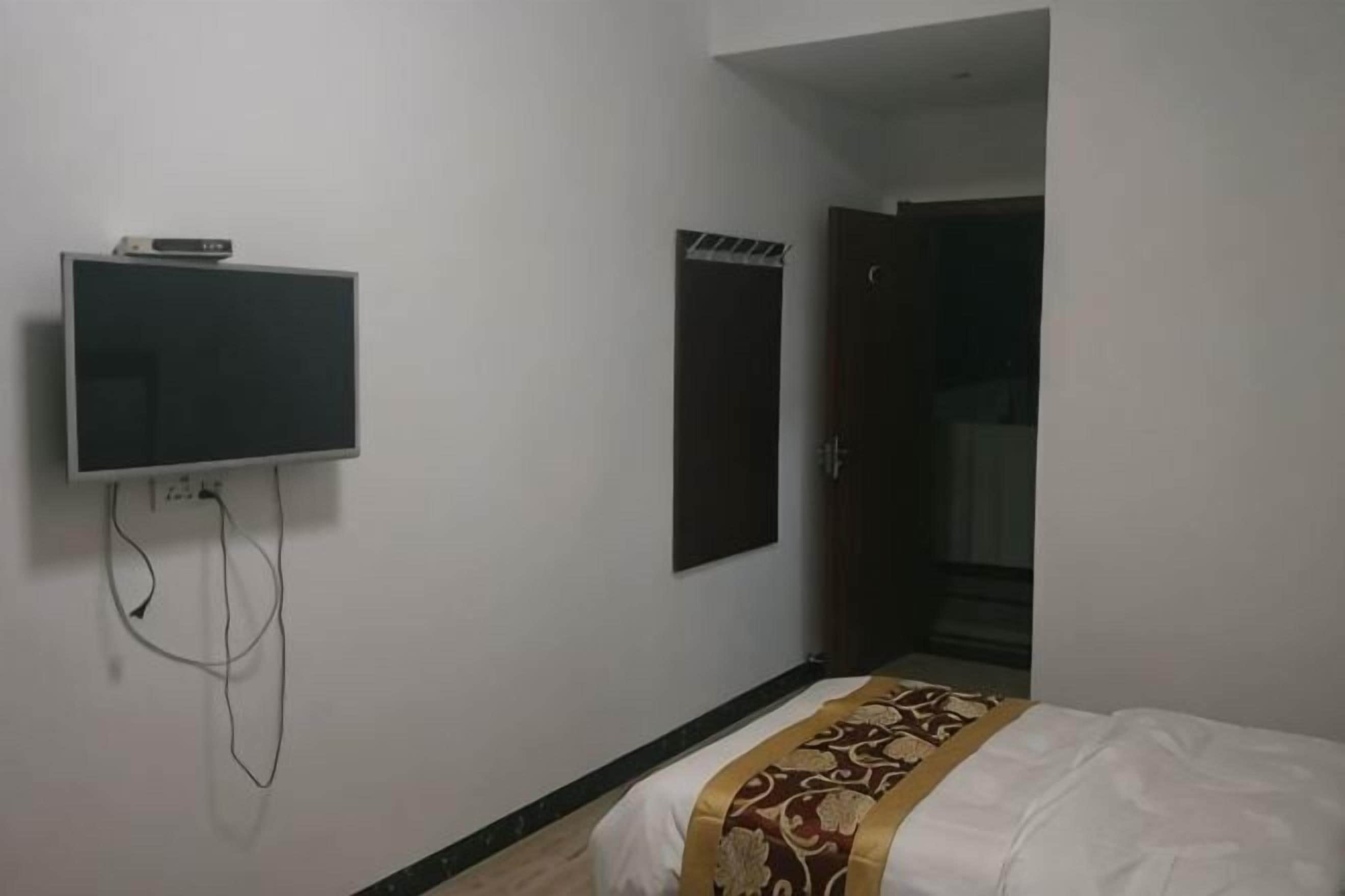 A room with a bed, a television mounted on the wall, and a door leading to another room.