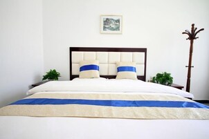Una cama bien hecha con colcha blanca y azul, un cabecero de madera y dos mesitas de noche con plantas.