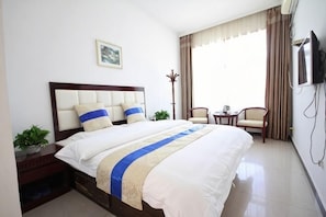 A hotel room with a bed, a TV, a chair, a small table, and a window with curtains. - Yuquan Hotel (Huayin)