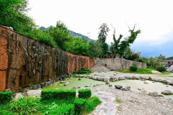 A stone pathway leading to a staircase, surrounded by greenery and a decorative wall. - Yuquan Hotel (Huayin)