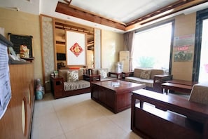 A living room with a sofa set, a coffee table, and a TV. There is a sliding door leading to another room. - Yuquan Hotel (Huayin)