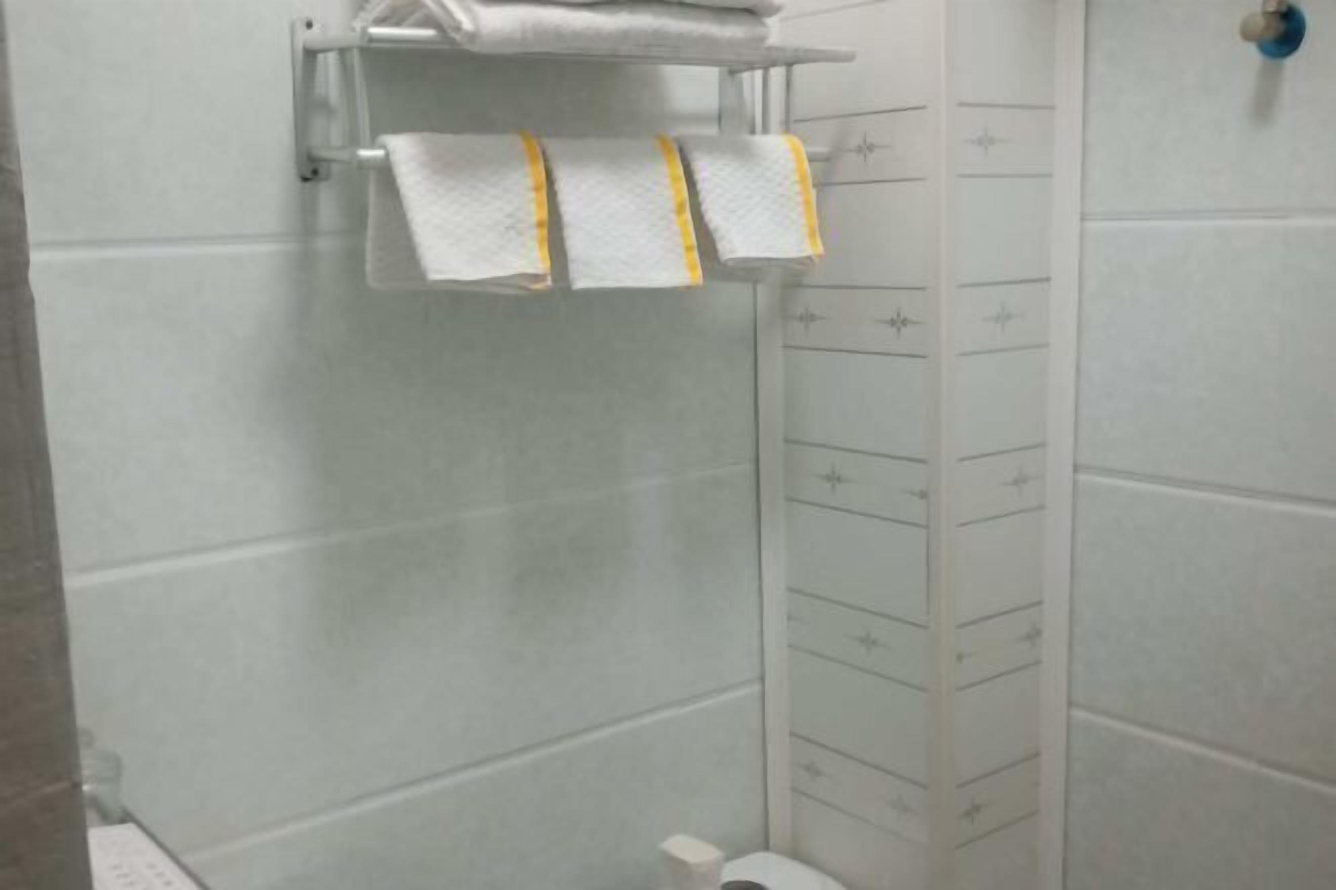 A bathroom with white tiled walls, a white towel rack with two towels, and a toilet.