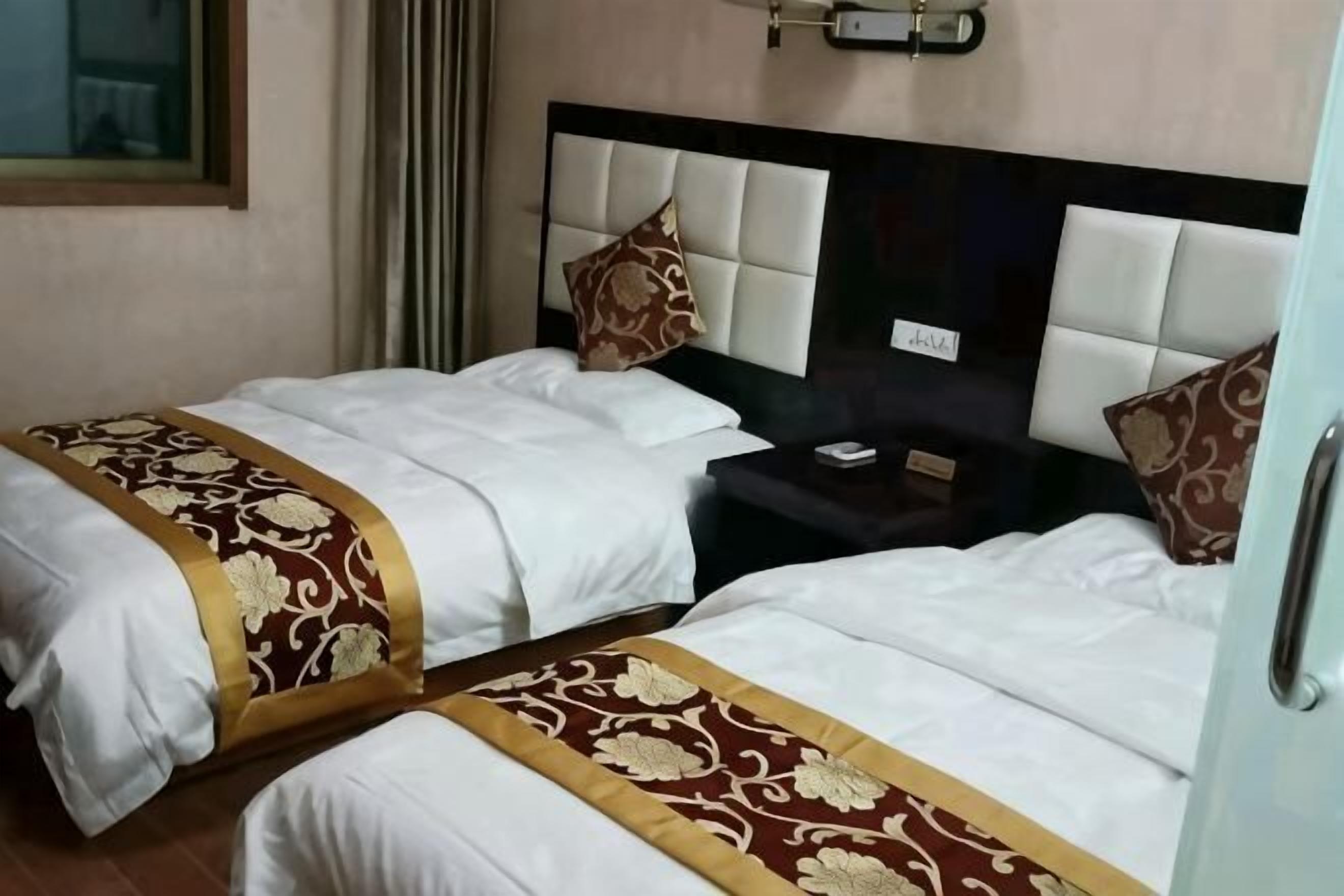 Deux lits avec du linge de lit blanc orné de motifs dorés, une tête de lit avec une plaque nominative et une table de chevet avec un téléphone.