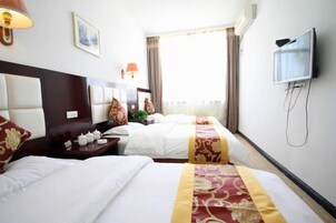 Una habitación de hotel con dos camas, televisión, mesita de noche con lámpara y ventana con cortinas.