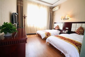 Habitación de hotel con dos camas, un aparador de madera, una planta en maceta y una ventana con cortinas.