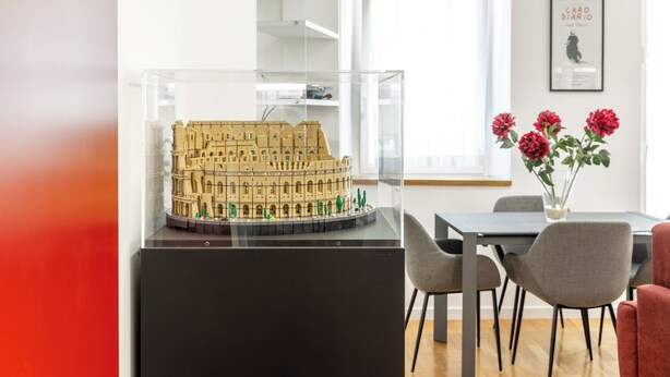 A model of a historical building displayed in a clear case, with a dining area featuring a table, chairs, and a vase of flowers in the background. - Saint Peter House Station Deluxe (Roma)