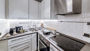 A modern kitchen with white cabinets, a stainless steel range hood, and a black induction cooktop. - Saint Peter House Station Deluxe (Roma)