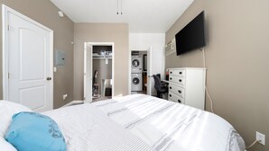 Ein Schlafzimmer mit einem Bett, einem Deckenventilator, einer Waschmaschine und einem an der Wand montierten Fernseher.