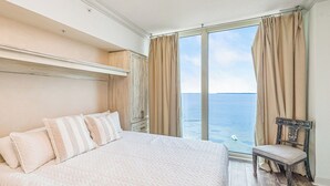 Ein Schlafzimmer mit einem großen Bett, einem Sessel und Meerblick durch ein Fenster.