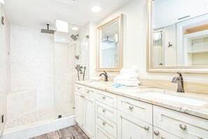 Un baño con ducha compartimentada por vidrio, tocador con lavamanos y dos espejos.