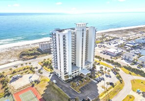 A high-rise hotel with multiple floors, a parking area, and a beach view.