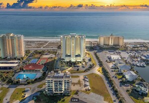 An aerial view of a coastal hotel complex with multiple buildings, a swimming pool, and a beach in the background.